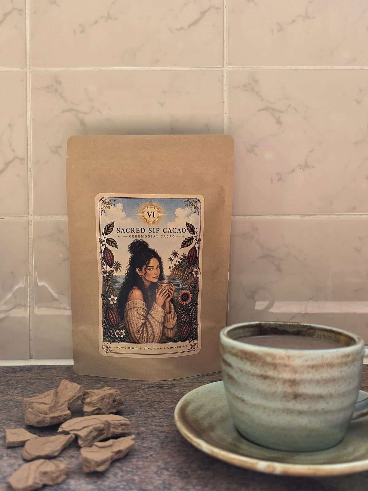 Sacred Sip Cacao pouch on a kitchen surface with pieces of cacao paste and a full mug of prepared cacao