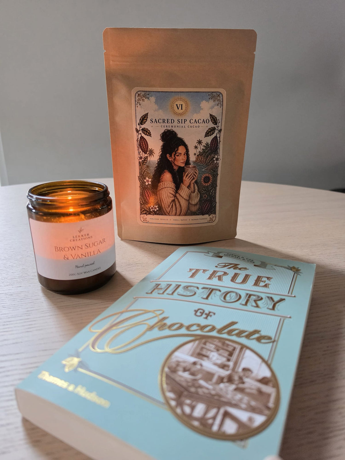 Sacred Sip Cacao pouch beside a lit candle and a book about the history of chocolate